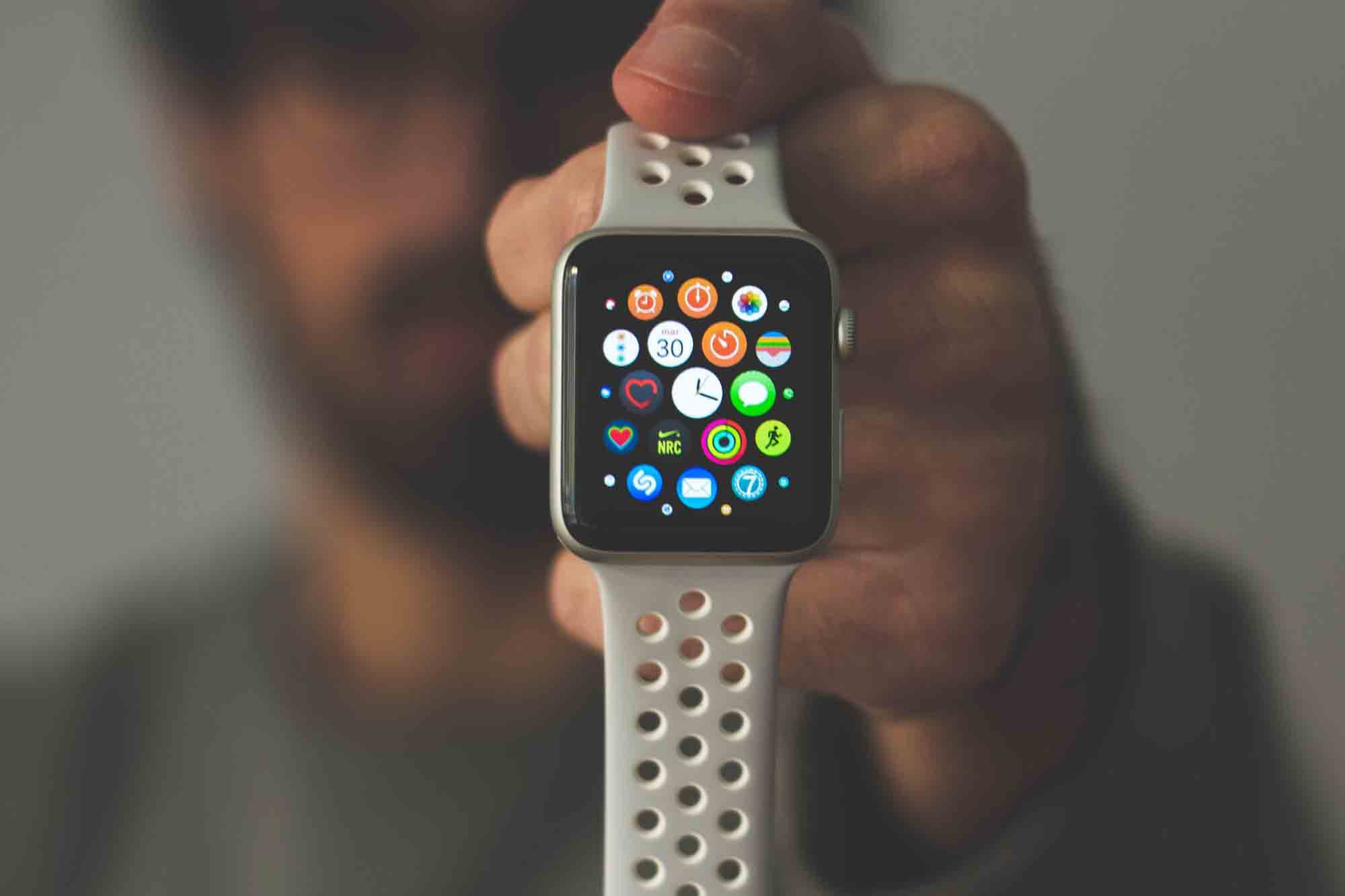  Male holding silver aluminum Apple Watch displaying apps with white Nike Sport Band, vertically in one hand