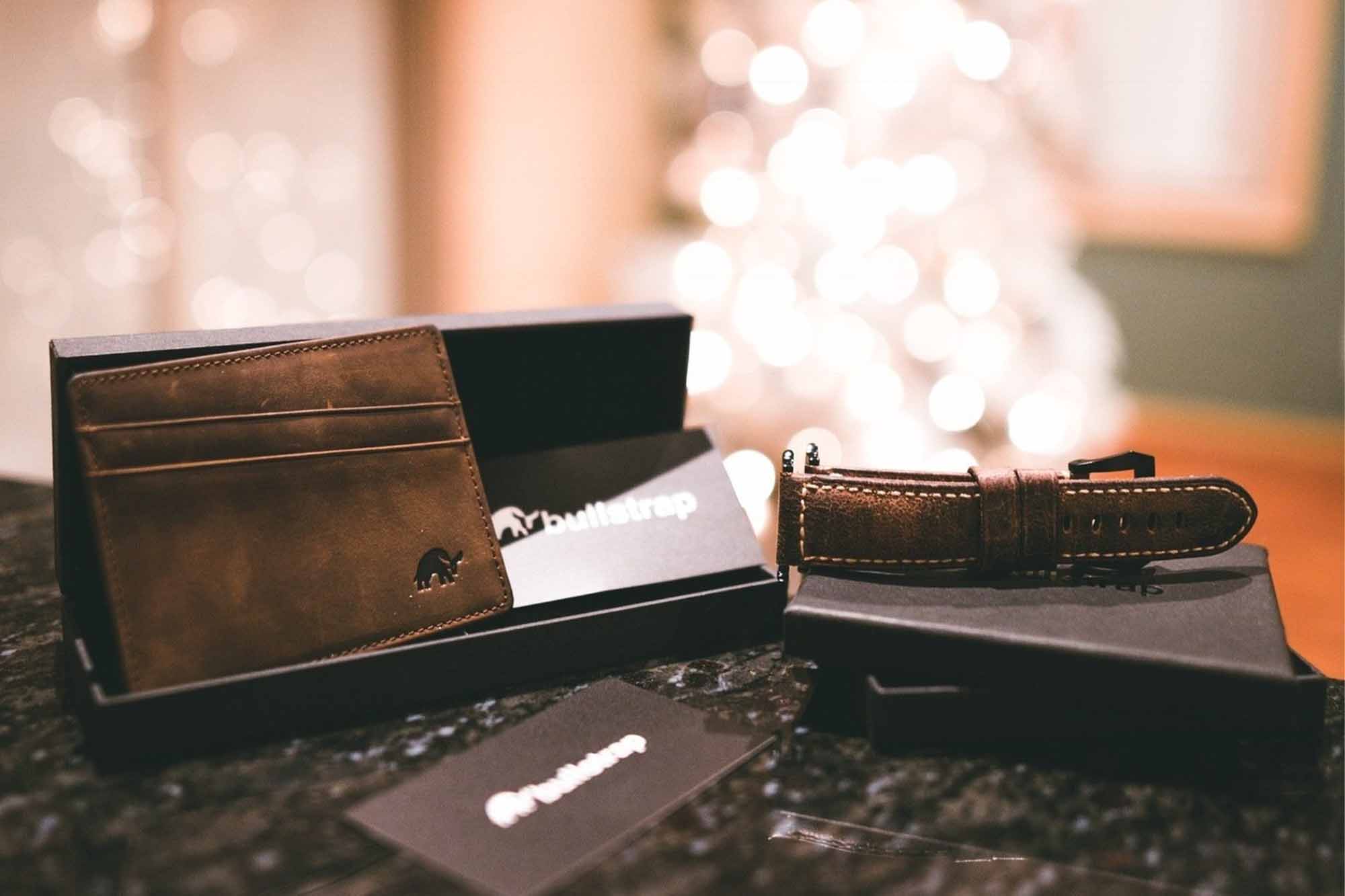 A Bullstrap leather Apple Watch band, leather wallet, and gift cards in focus with a lit Christmas tree in the background.