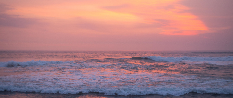 A serene ocean view at sunset with pink and orange hues in the sky.