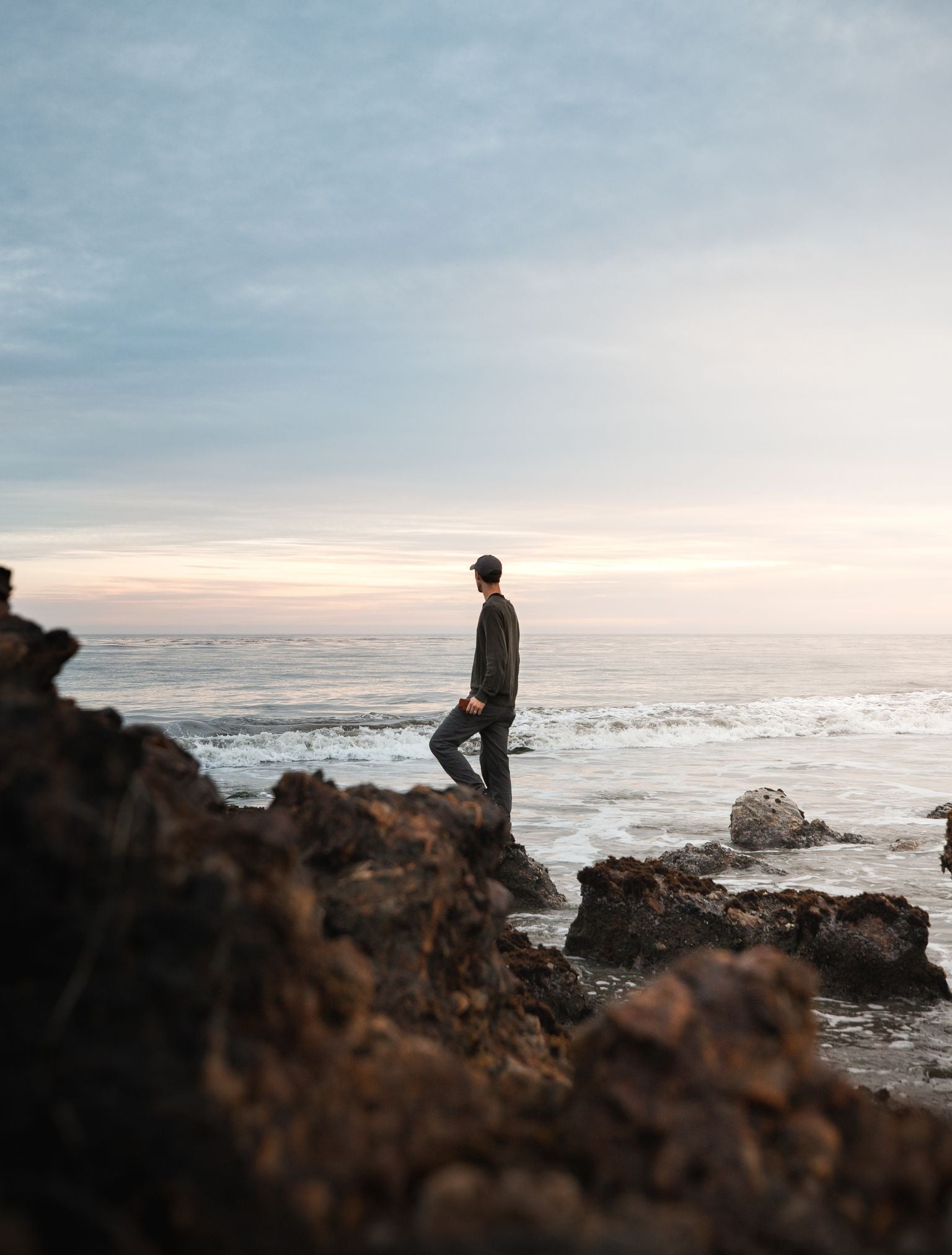 A person standing on rocks by the ocean during sunset