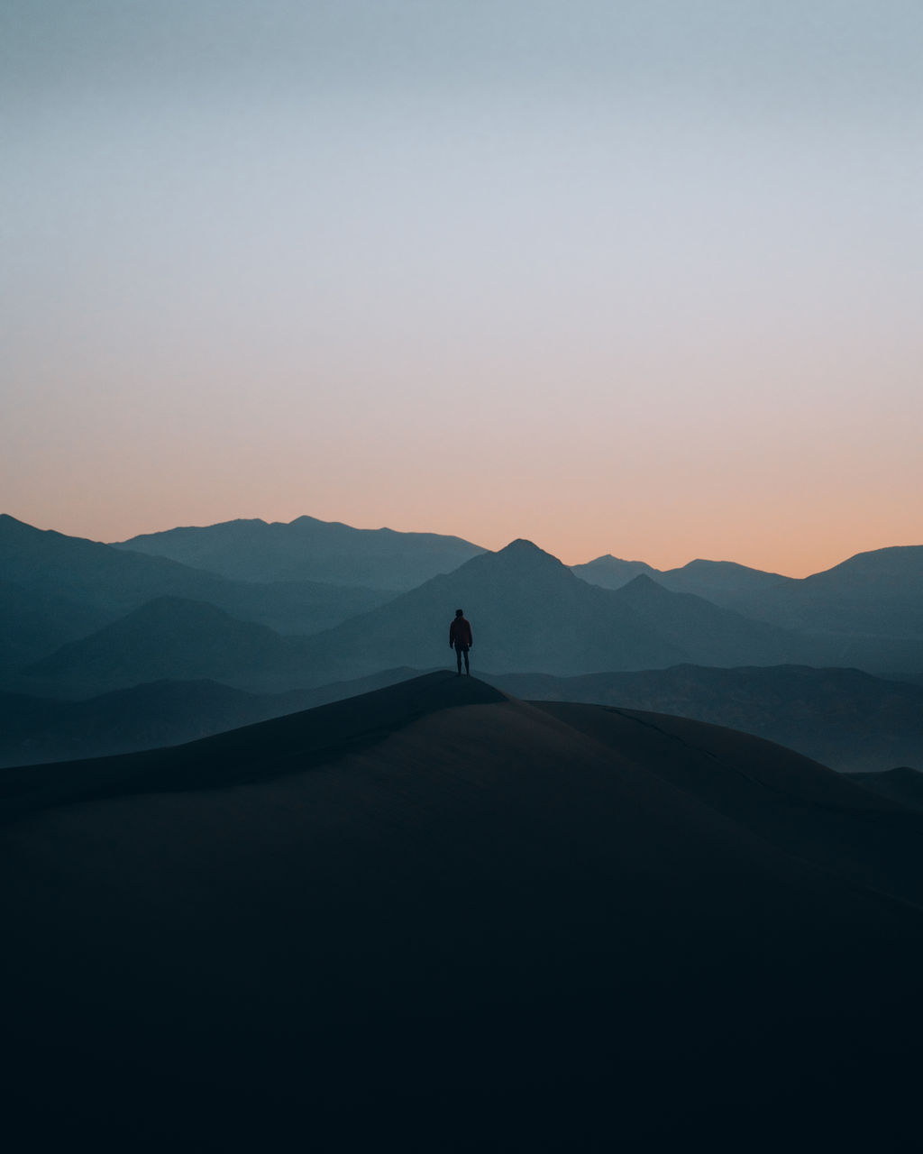 A person standing on a hill with mountains in the background during sunset