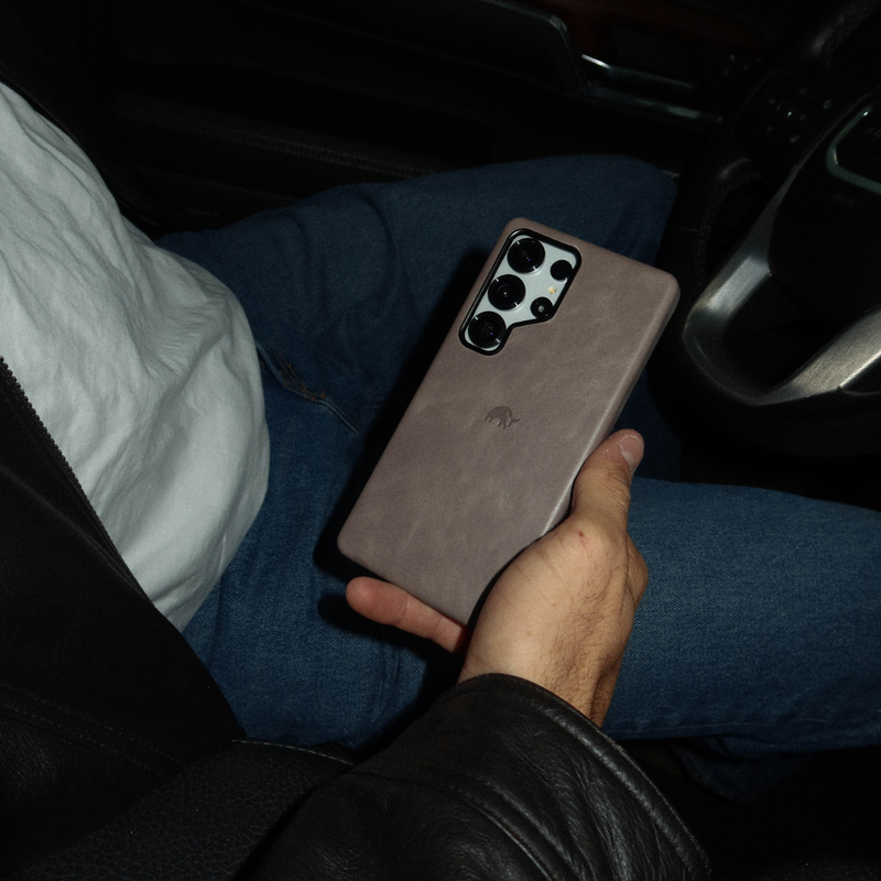 Back view of Samsung Galaxy S25 Ultra slate leather case showcasing camera cutout and embossed logo, held in a car interior