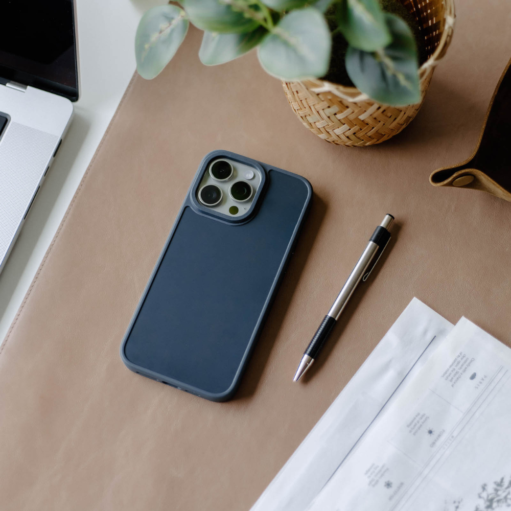 A navy phone case on a desk with a pen and plant nearby.