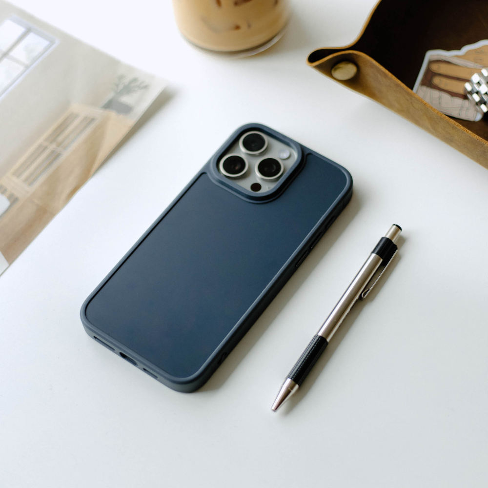 A navy blue phone case for iPhone with camera cutout, placed next to a pen on a table.