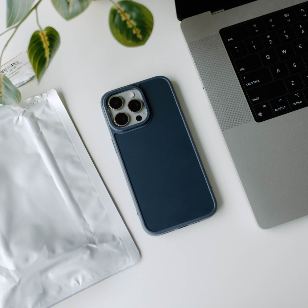 A navy phone case on a desk next to a laptop and packaging.