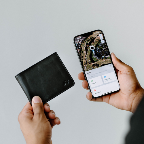A person holding a black leather bifold wallet and a smartphone displaying a map.