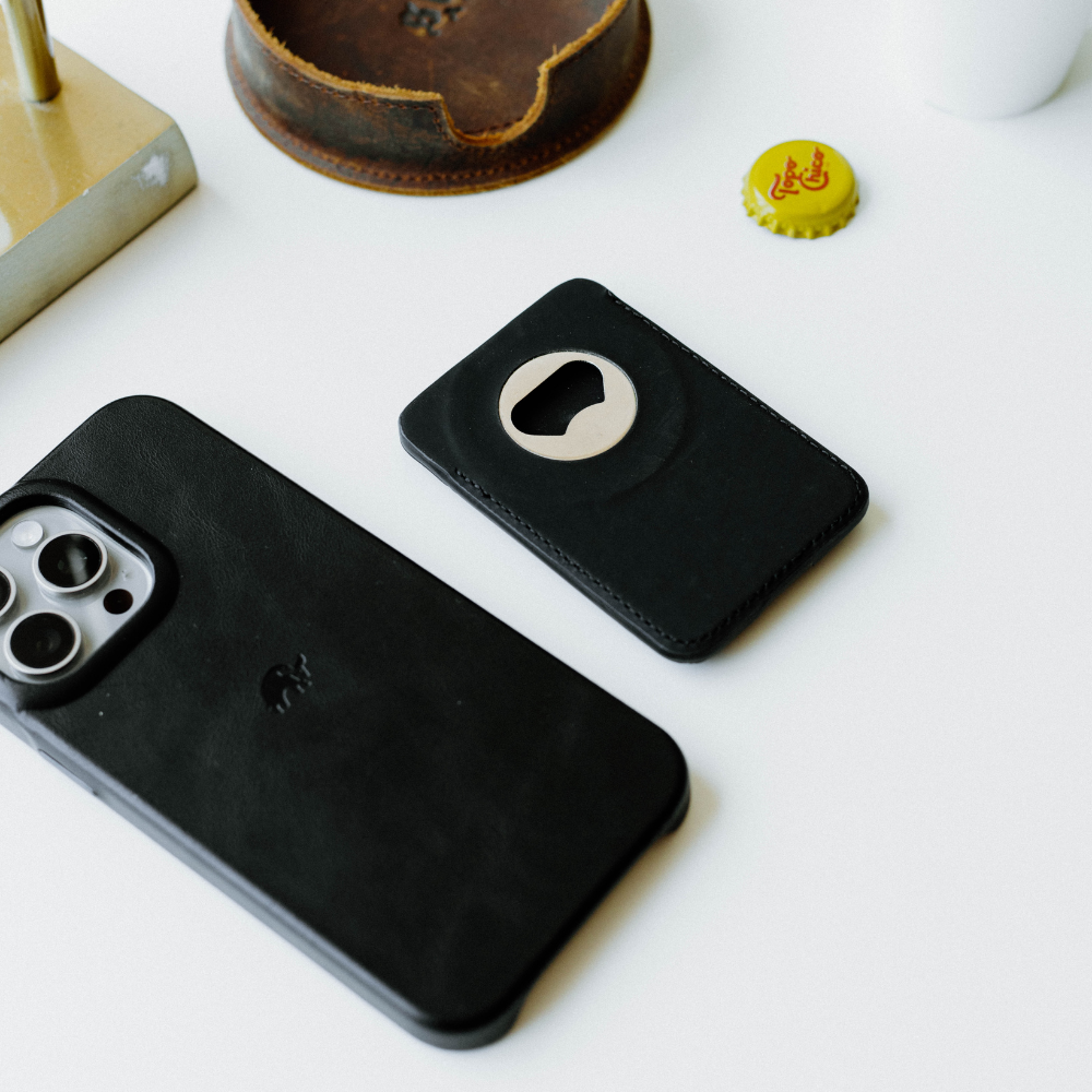 Black Magnetic Popper wallet on white desk beside matching phone case and yellow bottle cap reading 'Topo Chico'