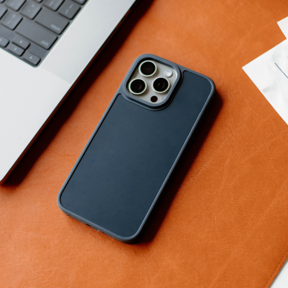 A navy phone case for an iPhone on a desk with a laptop