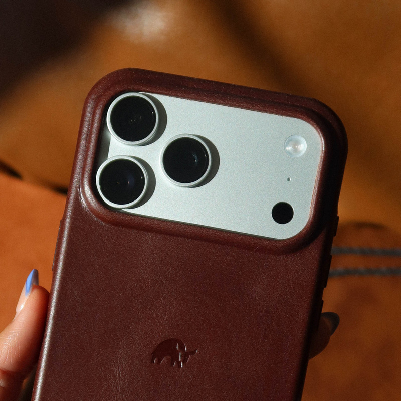 Close-up rear view of The Contemporary Plateau Case in Terra showcasing raised camera lip, burgundy leather texture and embossed rhino logo with warm brown background