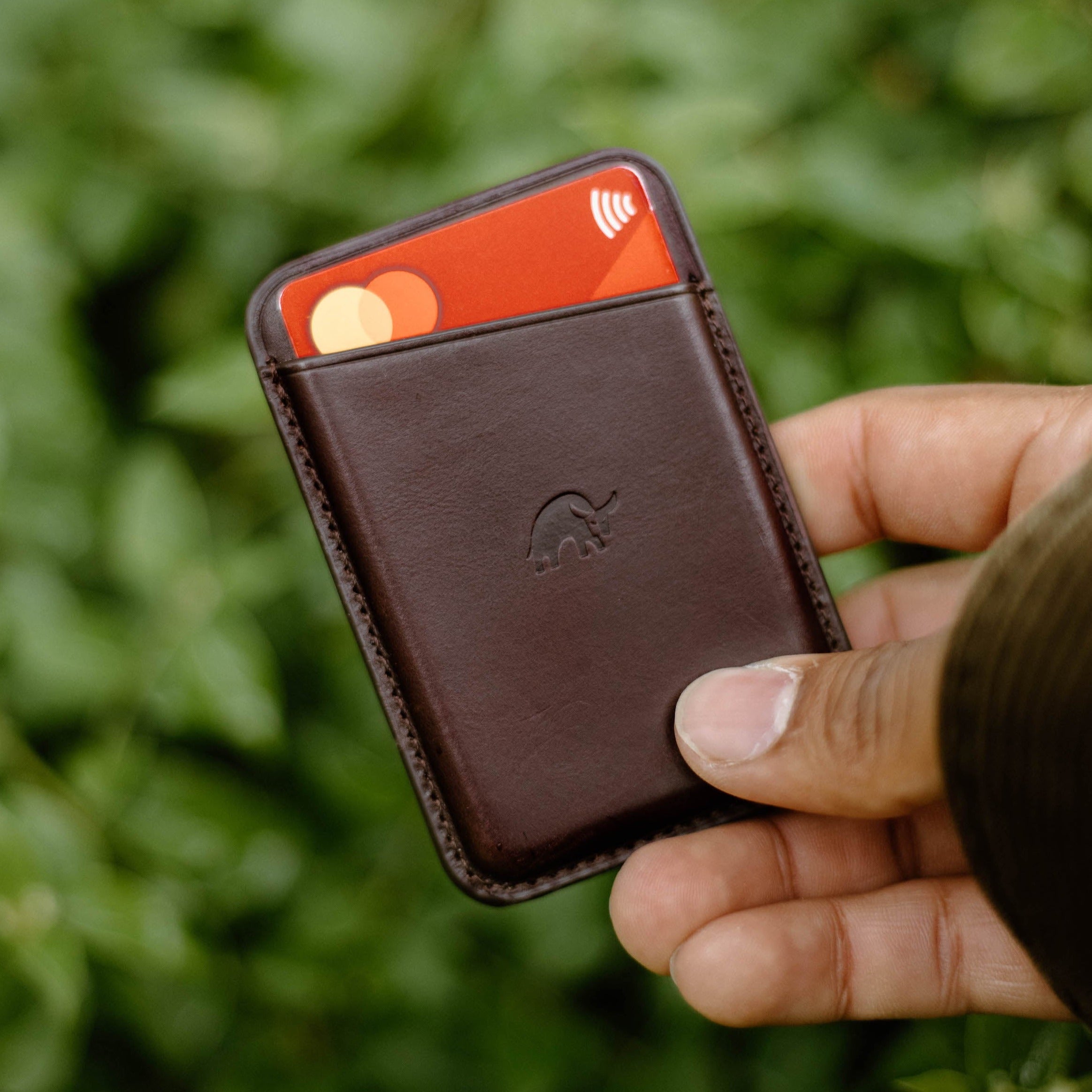 A hand holding a brown leather magnetic wallet with cards visible.