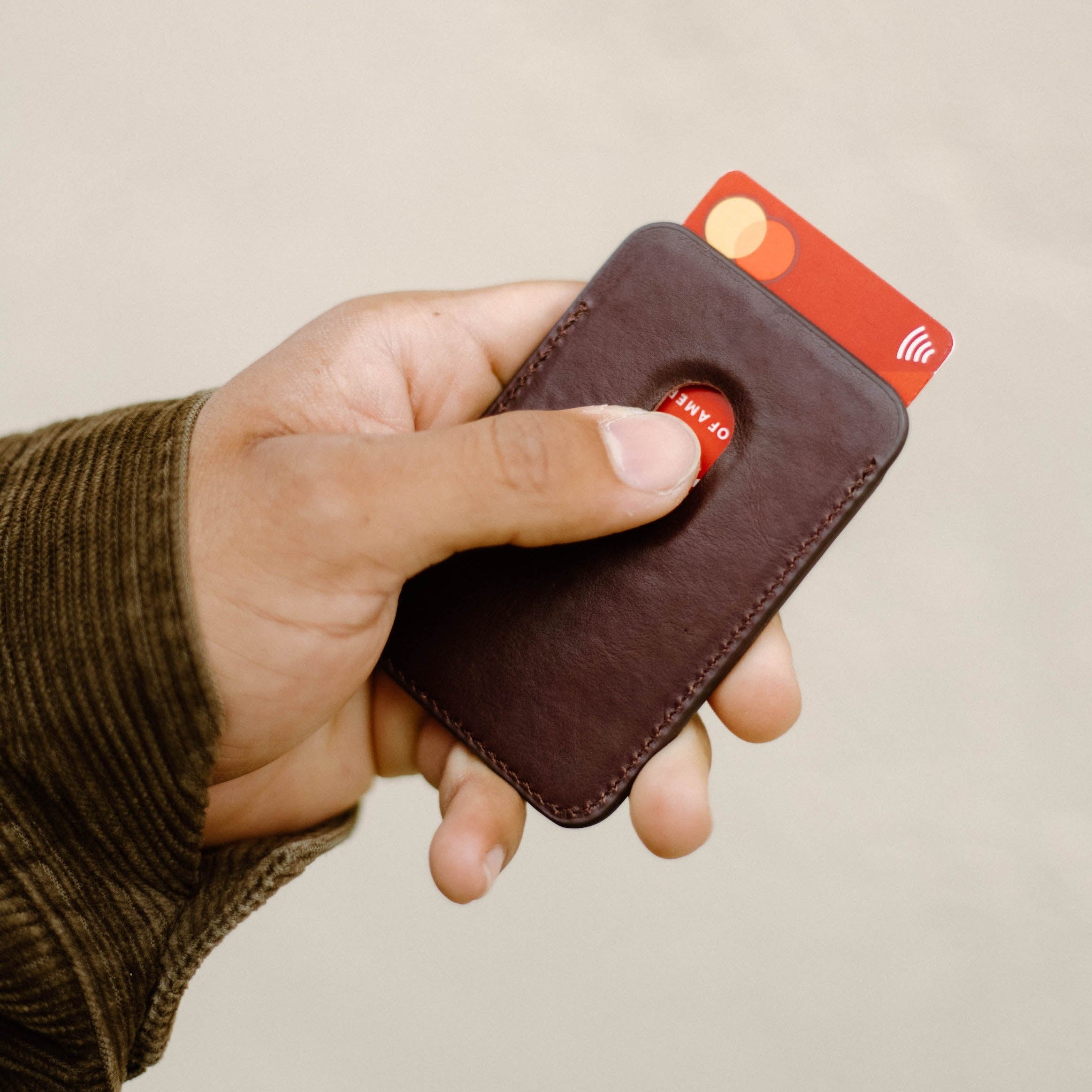 A person holding a Leather Magnetic Wallet in Bourbon color with a card partially visible.