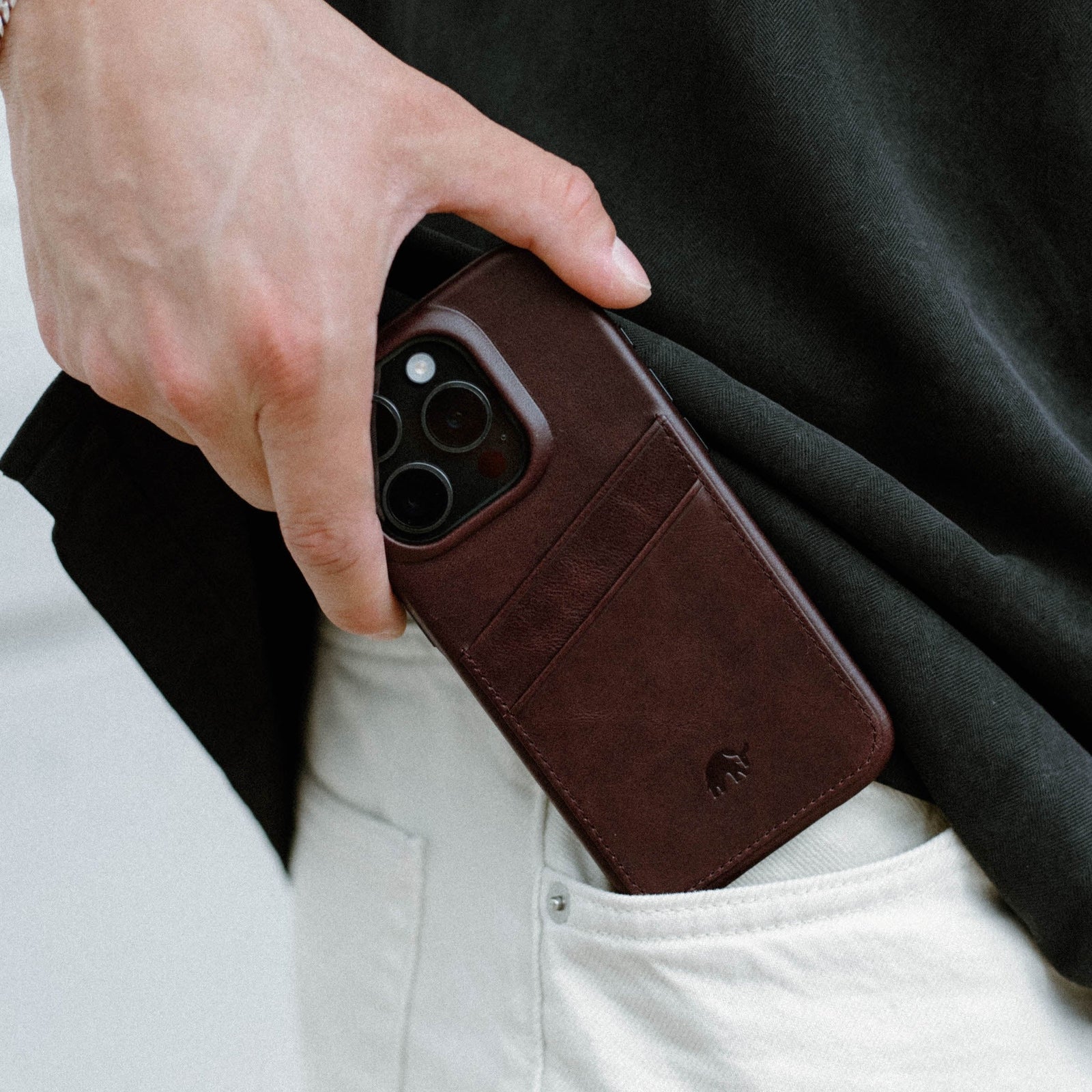 Brown leather phone wallet with card slots and small embossed elephant logo held at a pants pocket.