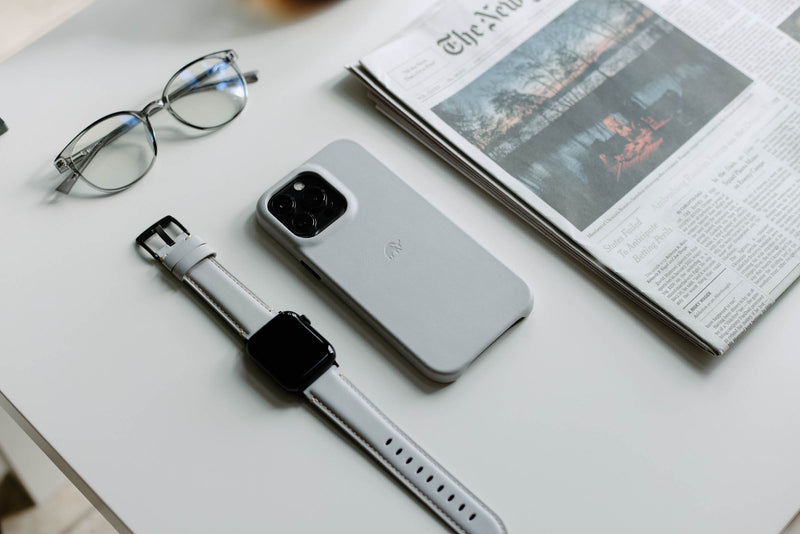Top-down view of Cloud MagSafe iPhone case showing camera cutout and embossed logo on a white desk with Apple Watch and newspaper