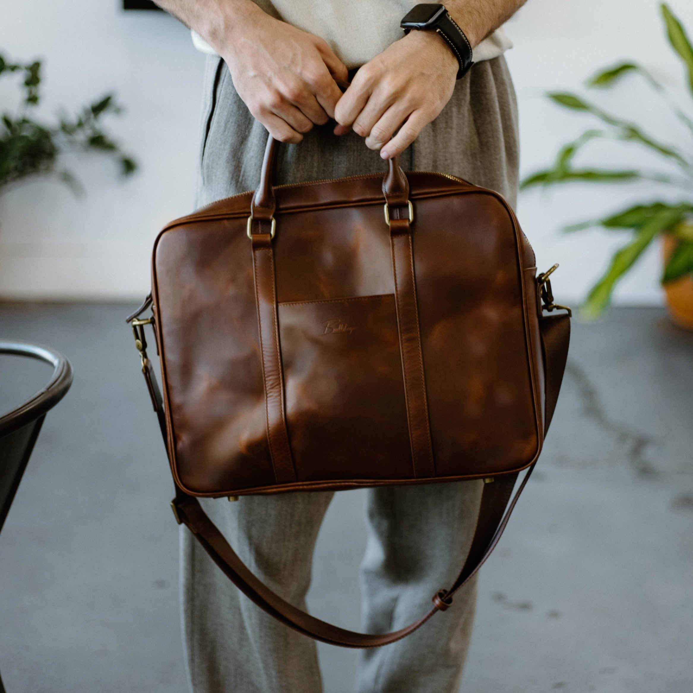 A person holding a brown leather bag, showcasing its design and functionality.