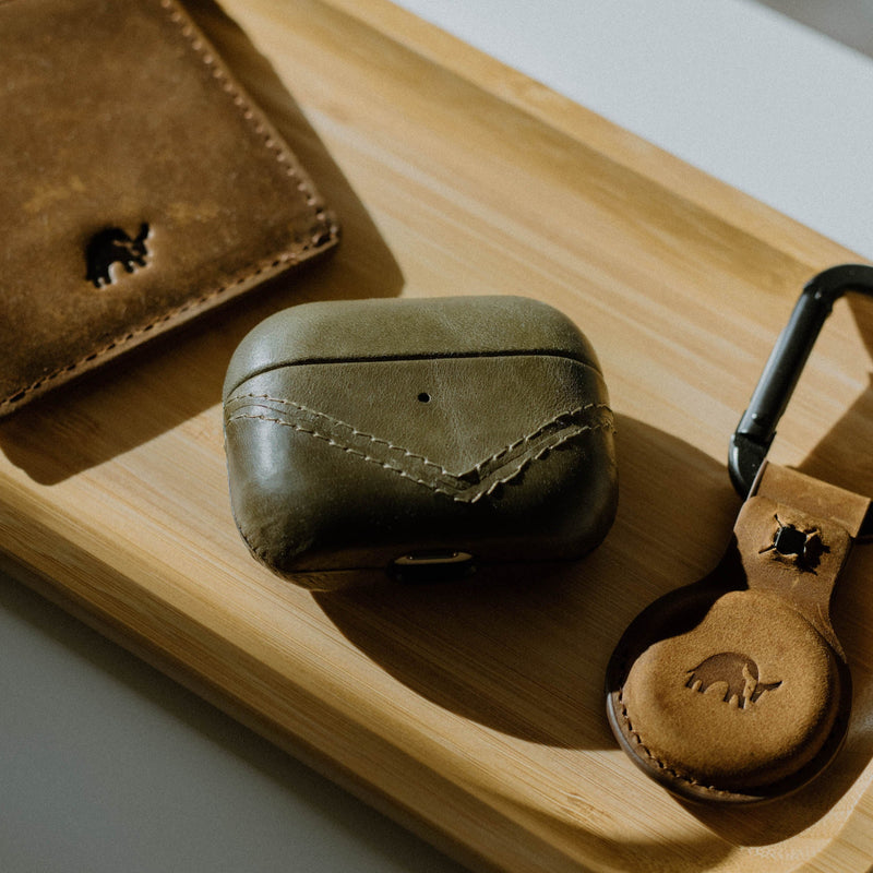 Leather AirPods case on a wooden tray with a wallet and keychain.
