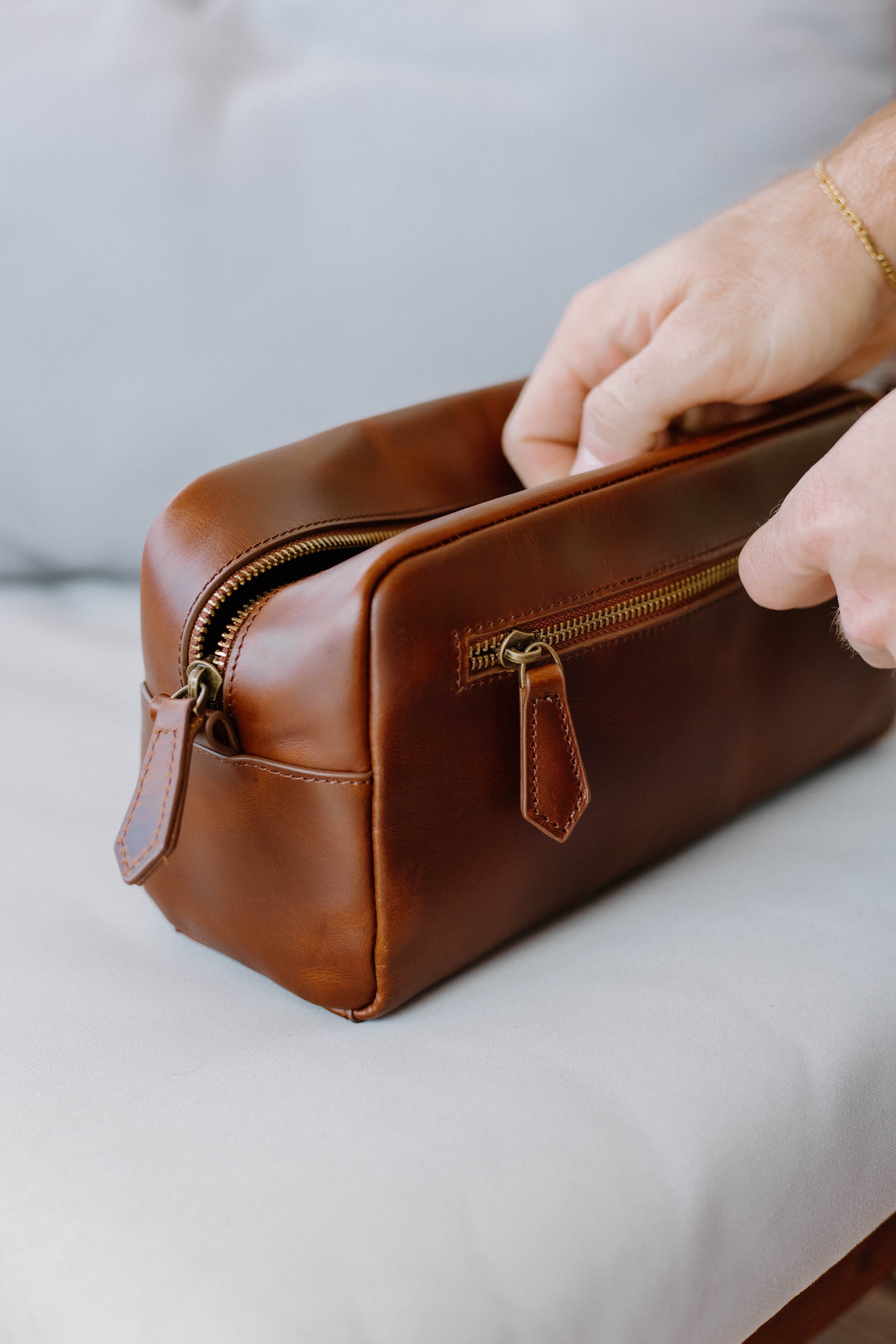 A person holding a brown leather toiletry bag with a zipper.
