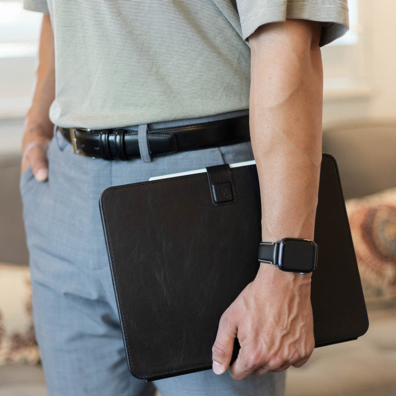 Person holding a black leather iPad case with strap closure and tablet peeking out, standing in a casual indoor setting