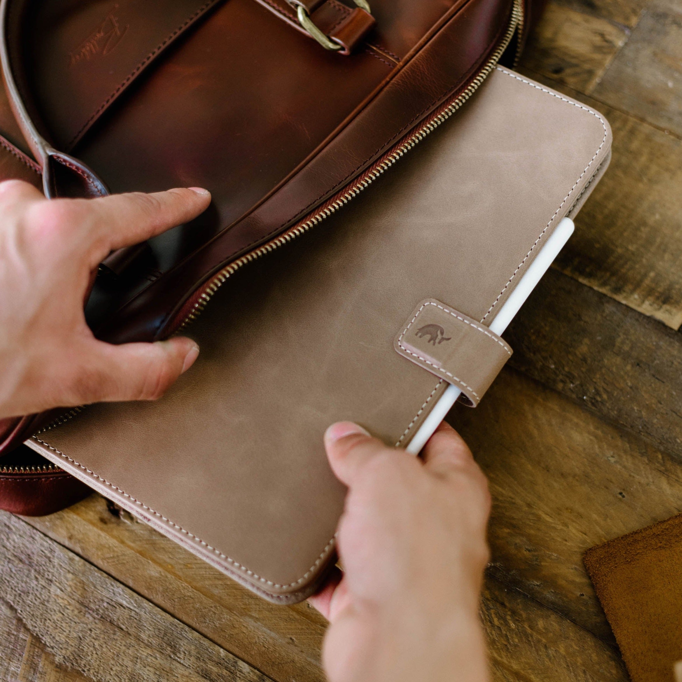 A person placing a Leather iPad Case - DUNE into a brown leather bag.