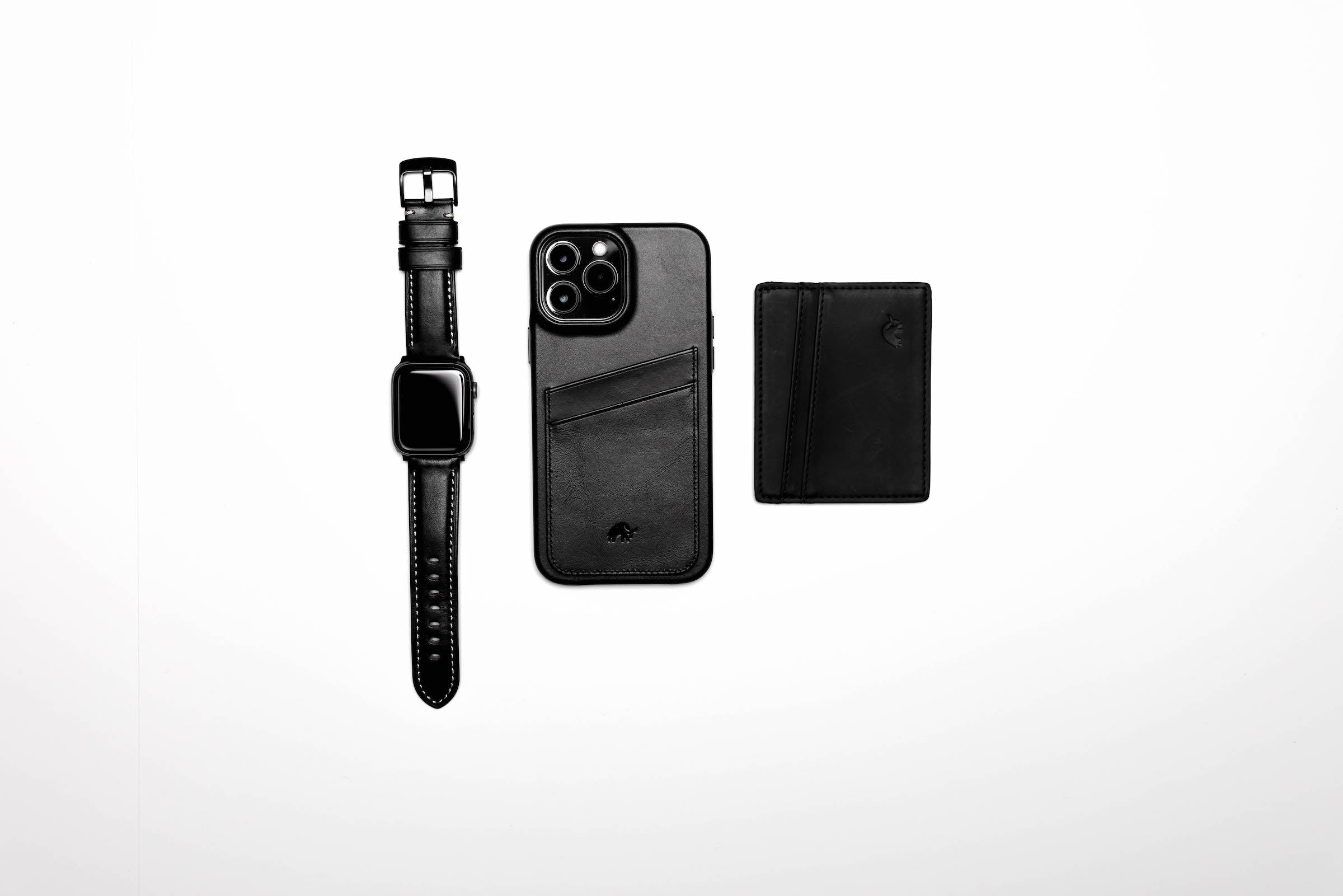 Black leather Apple Watch strap, phone case, and wallet arranged on a white background.