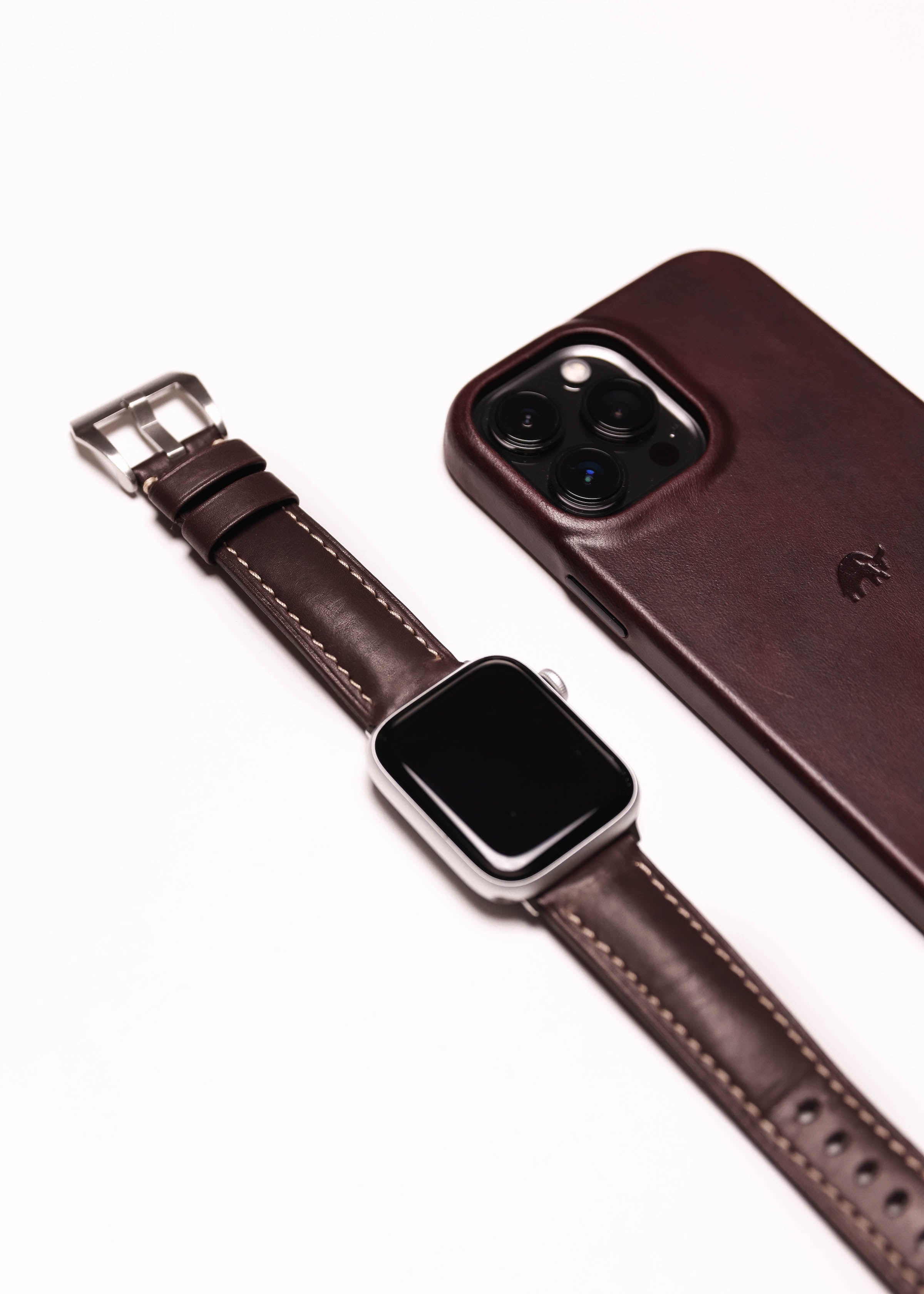 A leather Apple Watch strap in brown next to a brown phone case.