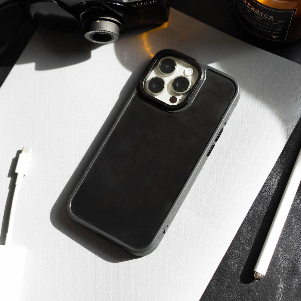 Black phone case on a white textured mat, iPhone camera corner visible, stylus and charging cable nearby.