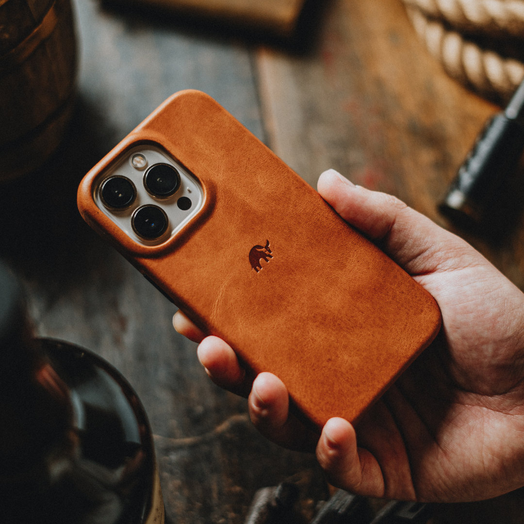 A hand holding a brown leather phone case with a logo on the back.