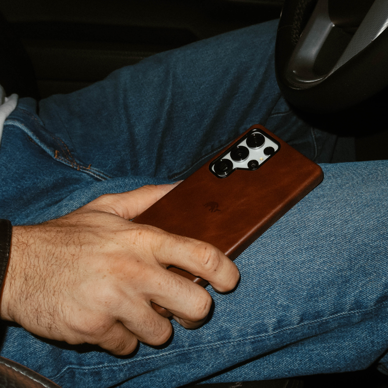 Angled view of Terra brown leather Samsung Galaxy S25 Ultra case showing camera cutout on a person's jeans-clad lap in a car