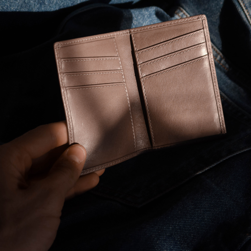 Hand holding open Leather Nav Messenger Wallet in slate showing interior card slots and bill pocket on denim background