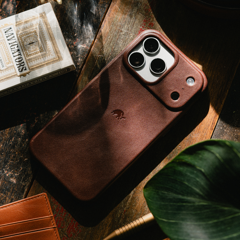 Angled back view of Terra leather MagSafe iPhone case showing raised camera cutout and embossed elephant logo on wooden table