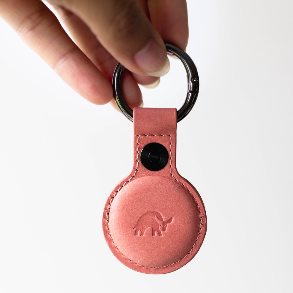 A pink leather AirTag holder with a keyring, featuring an embossed bull logo