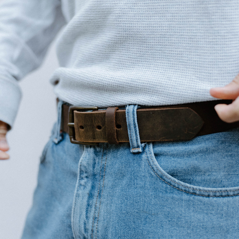 Close-up of Rugged Leather Belt Terra showing brass buckle and distressed brown leather on blue jeans