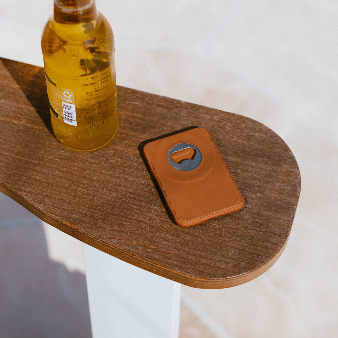 Sienna leather MagSafe wallet with round metal bottle opener on a wooden table beside a beer bottle