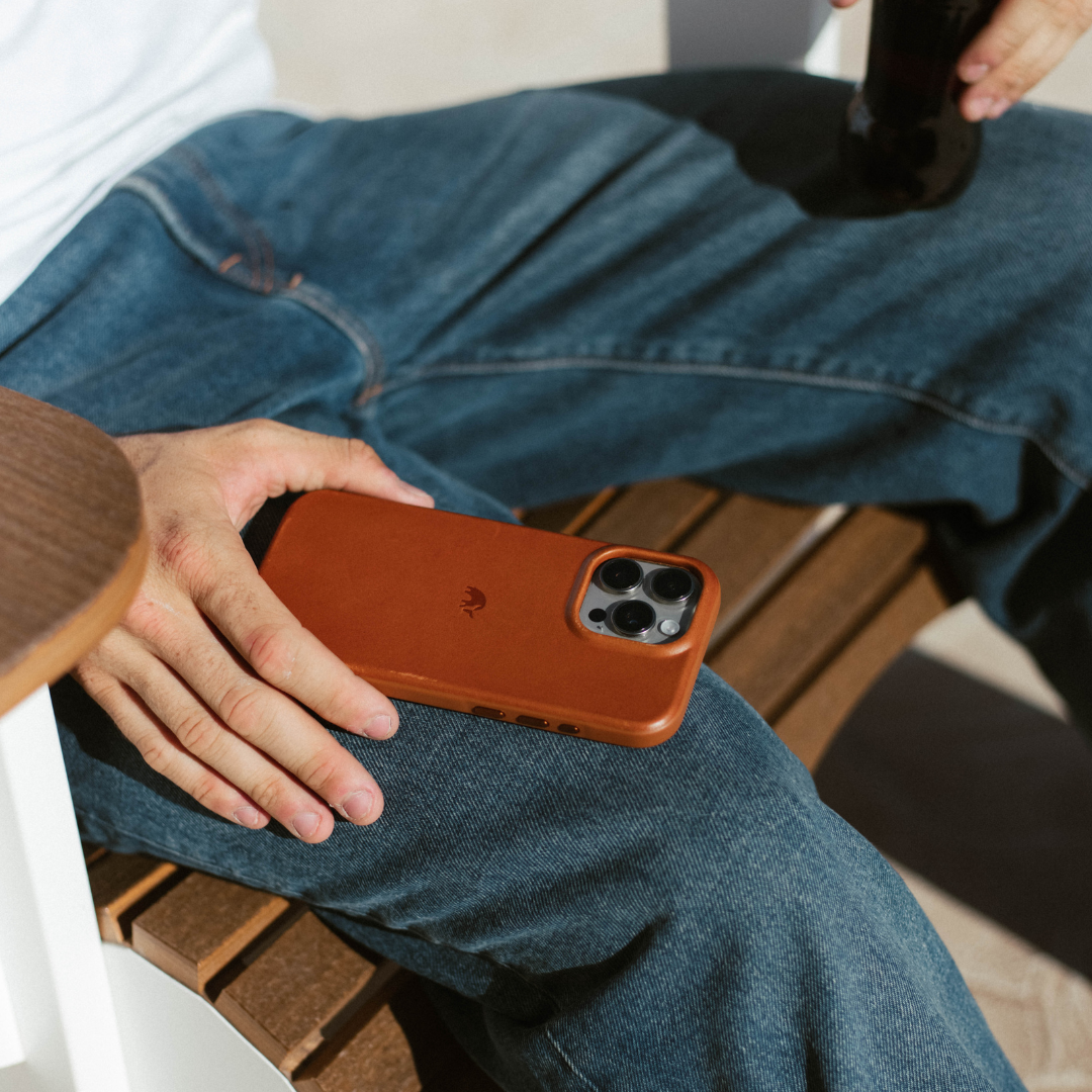 Brown sienna leather phone case resting on a person's denim-clad lap, phone camera lenses visible.