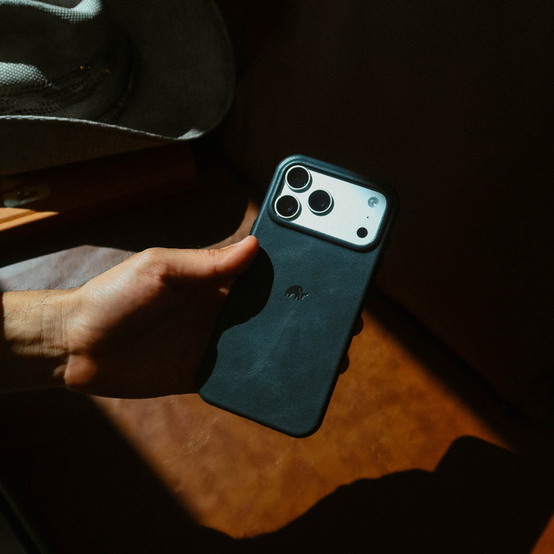 Hand holding Contemporary Plateau Case in Ocean showing leather back and raised camera plateau against sunlit leather