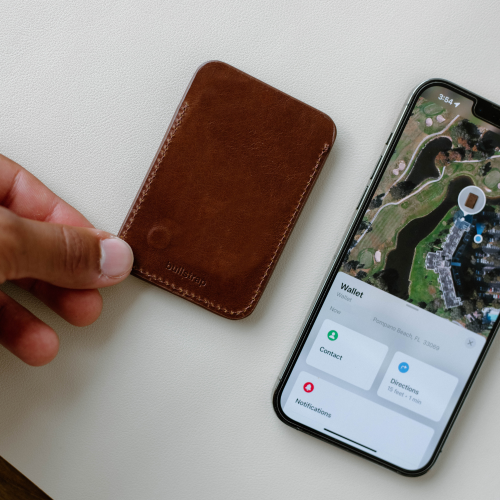 A hand holding a brown leather wallet next to a smartphone displaying a map.