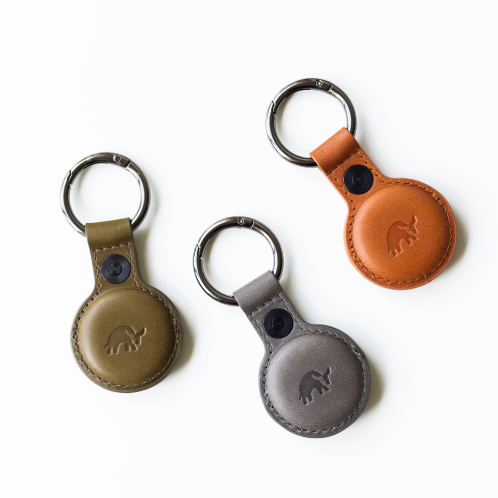 Three round leather key fob holders with metal rings in tan, olive, and slate, embossed bull logo