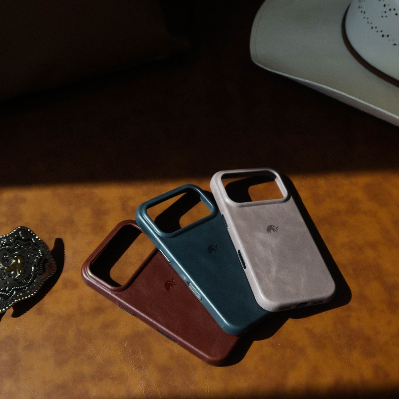Angled view of three Contemporary Plateau leather iPhone cases showing leather texture and raised camera ring on brown surface