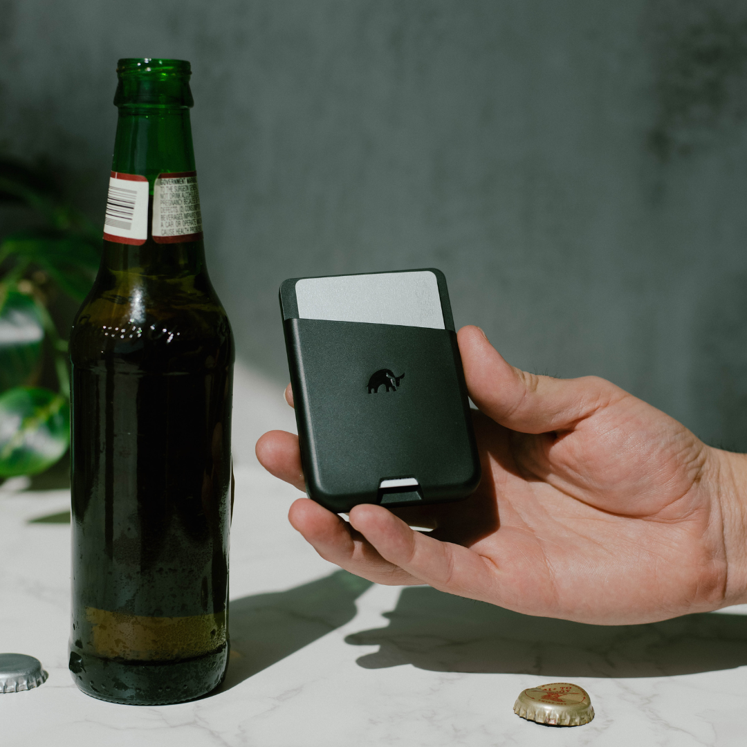 A hand holding the Magnetic Popper Wallet next to a bottle, showcasing its built-in bottle opener feature.