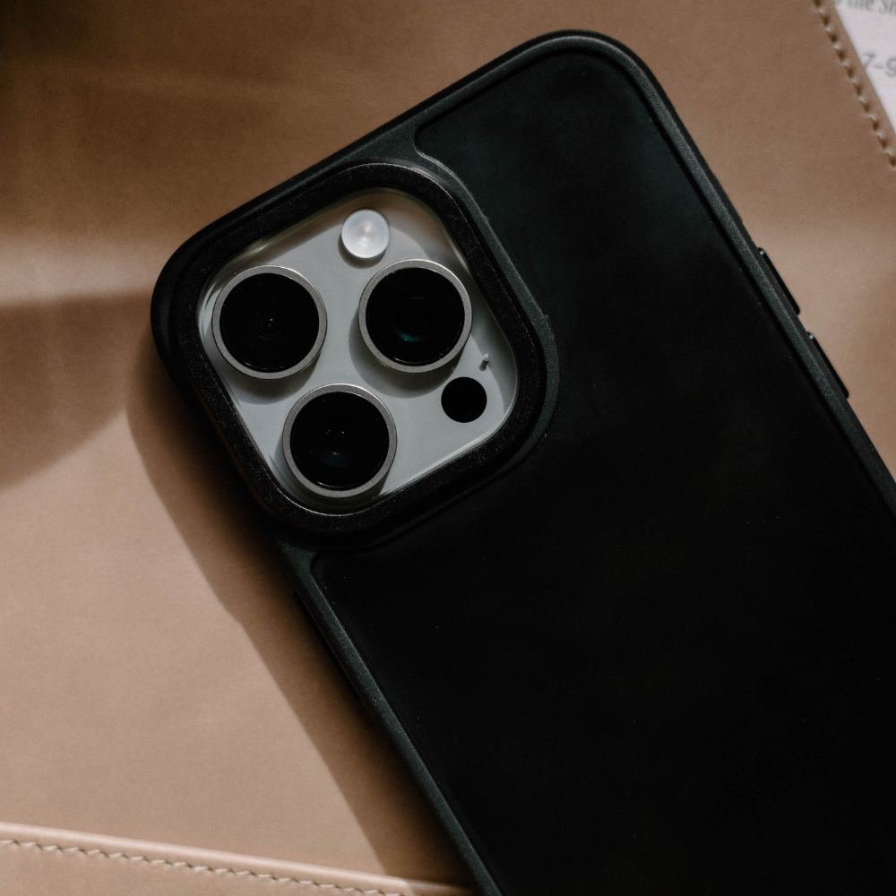 Black FRWD phone case (Abyss) showing the triple-camera cutout, placed on tan leather surface