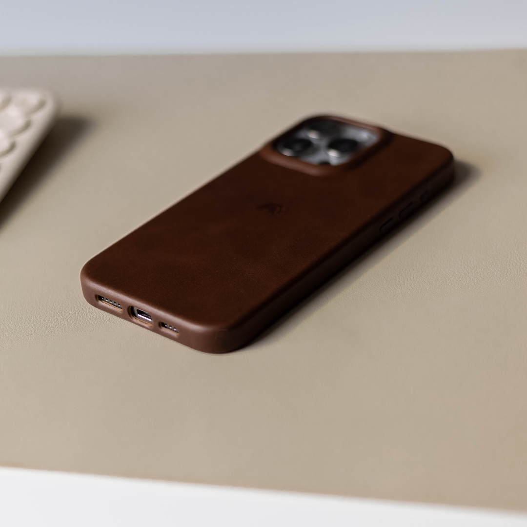 Brown leather iPhone case on a beige surface, showcasing the design and cutouts.