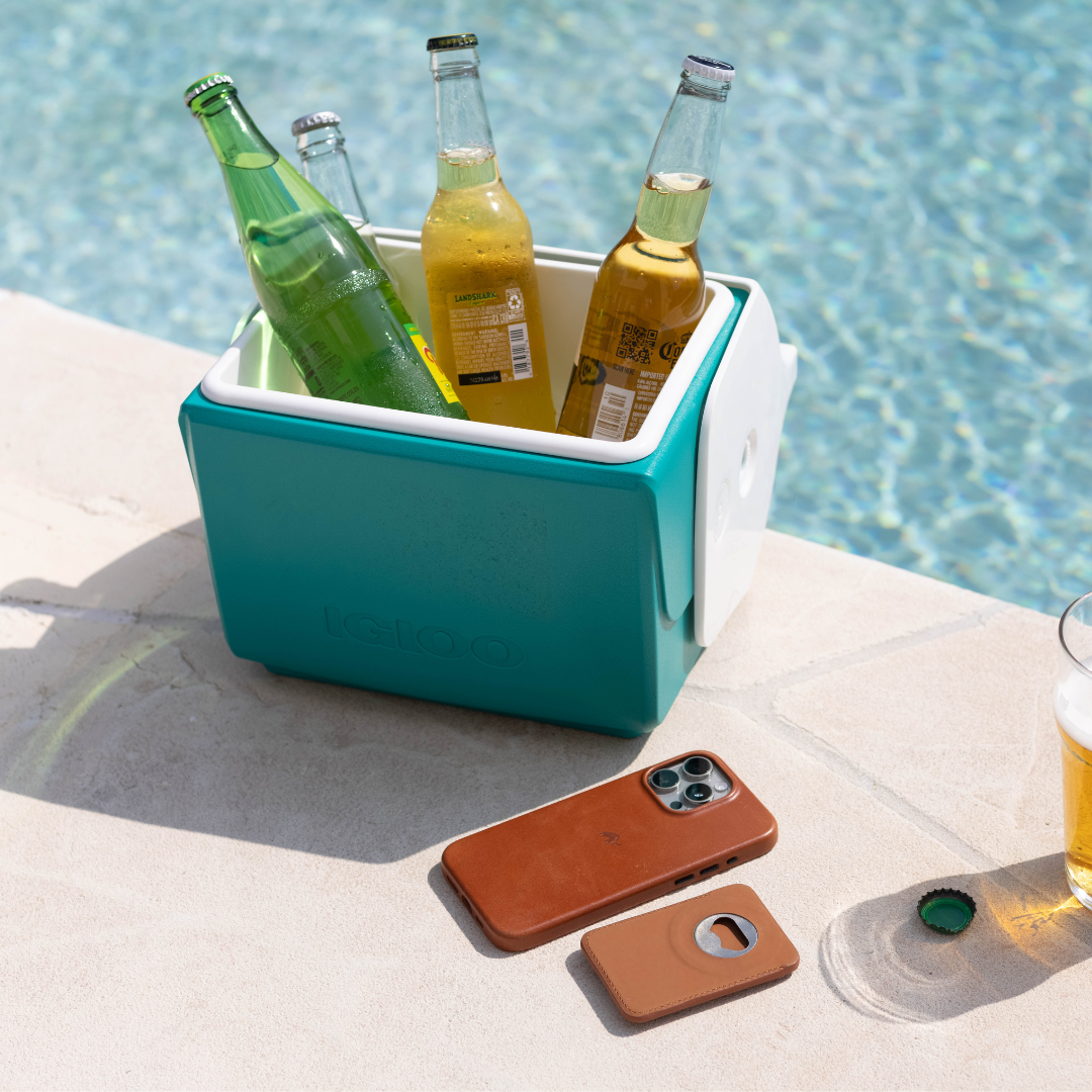 Teal IGLOO cooler by a pool holding bottles labeled LANDSHARK and Corona, leather phone case and wallet on pool deck.
