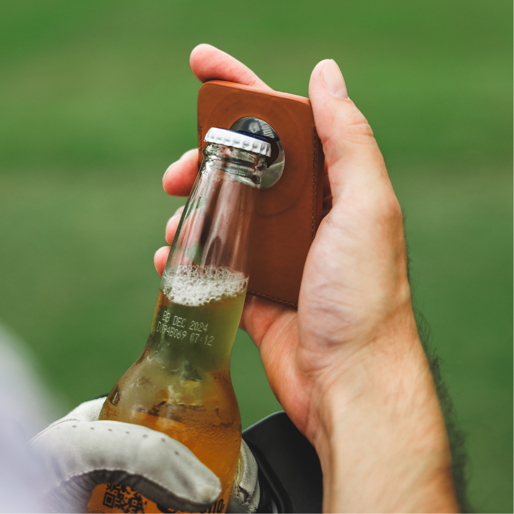 A person holding a leather magnetic wallet while holding a bottle of beer.