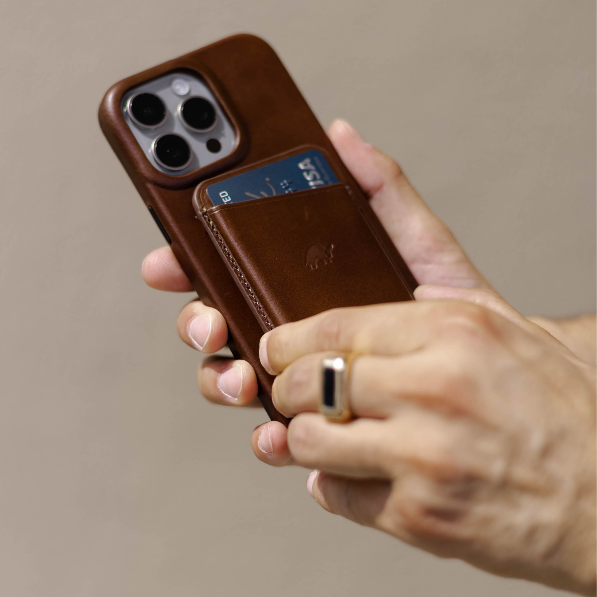 Brown leather phone case with attached card pocket holding a blue VISA card; hand holding case; visible text: ED