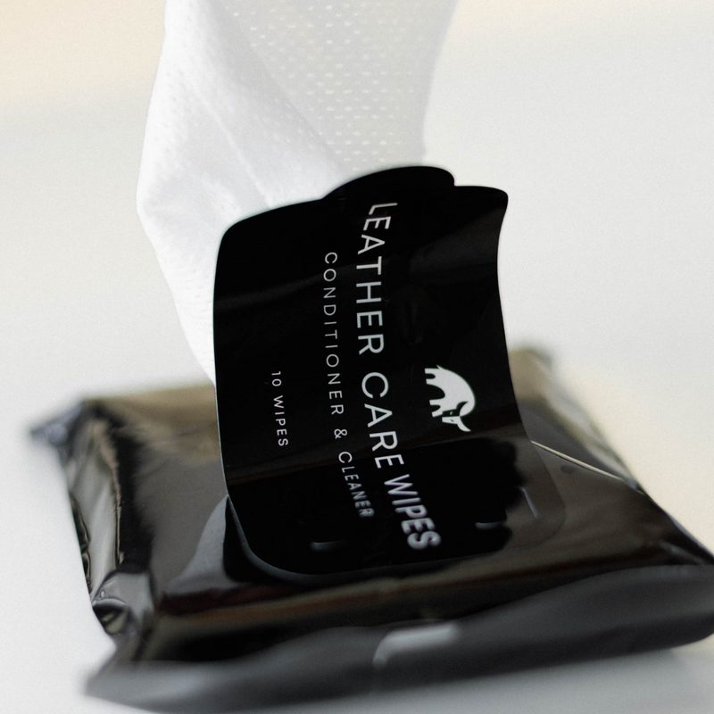Angled close-up of Leather Care Wipes pack with a wipe being pulled from the open lid, label visible, blurred white background