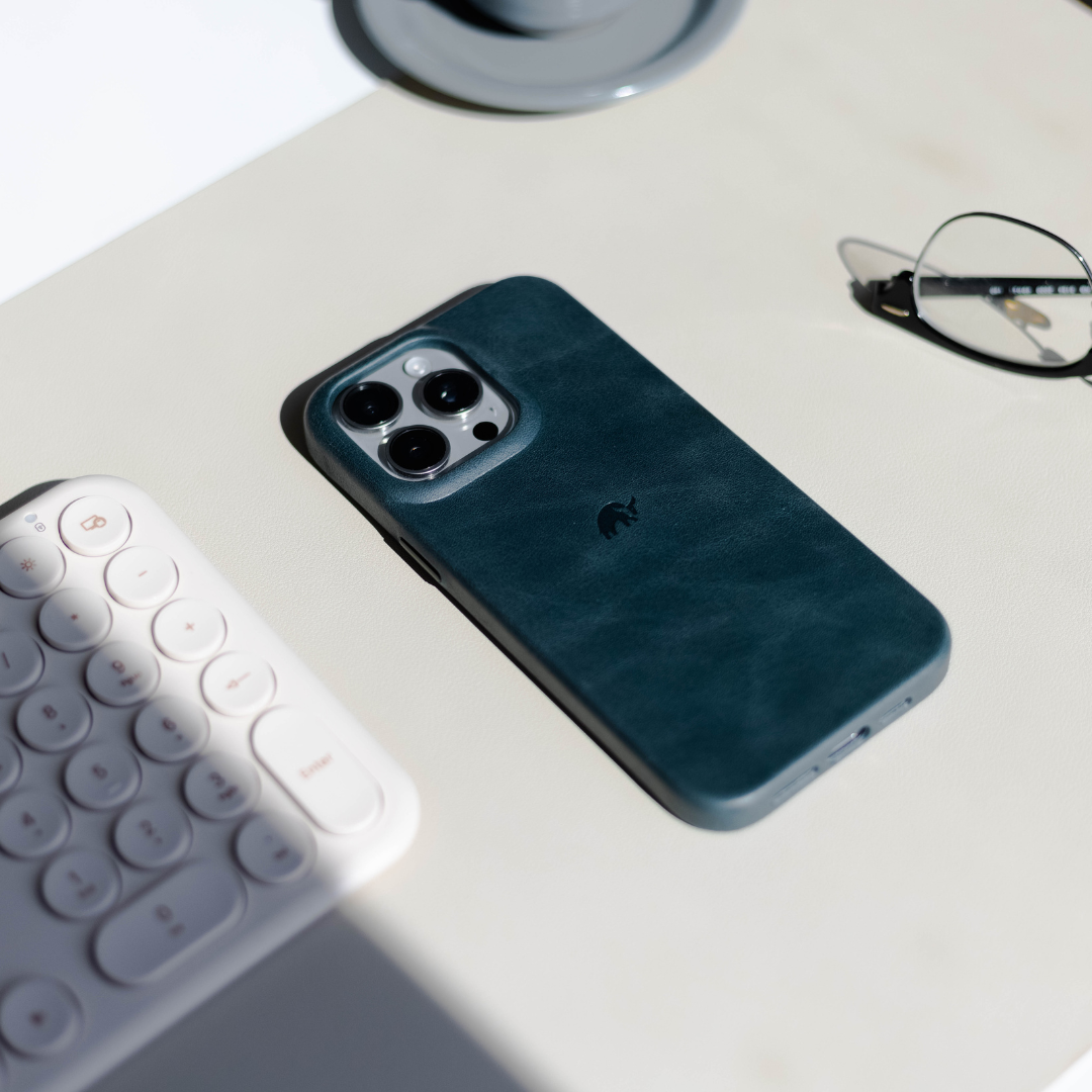 A teal phone case on a desk with a keyboard and glasses