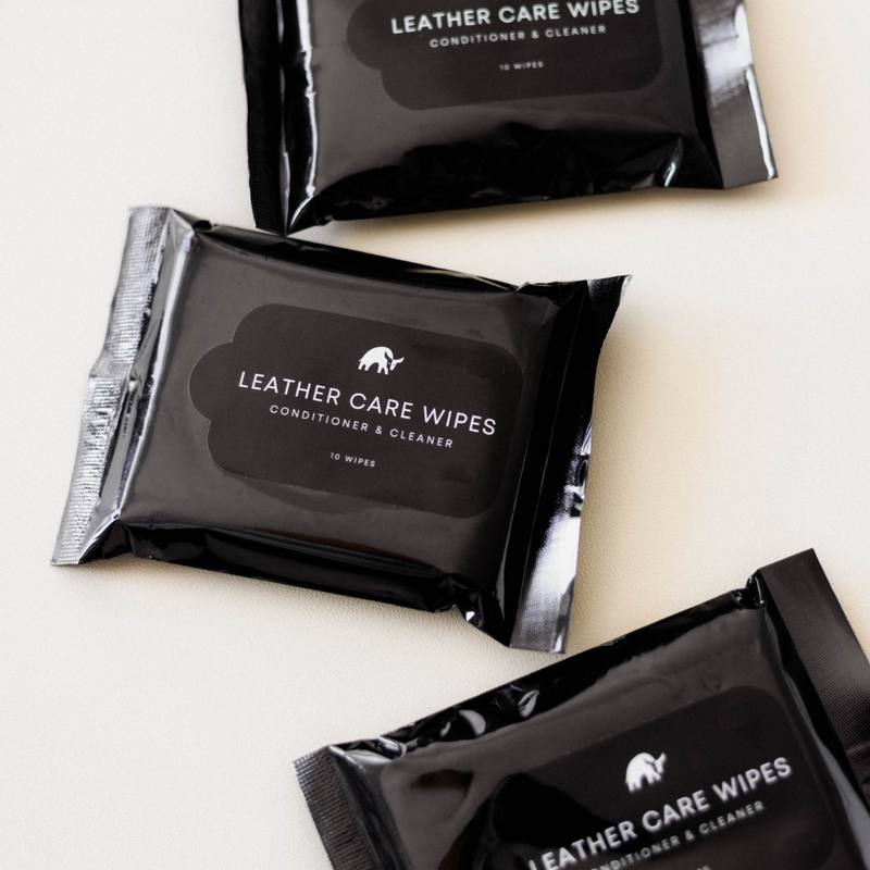 Angled flat-lay of three Leather Care Wipes packets with glossy black packaging and visible label 'LEATHER CARE WIPES' on a light background