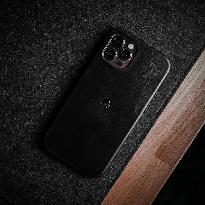Angled top-down view of Black Classic iPhone case showcasing embossed Bullstrap logo on felt and wood