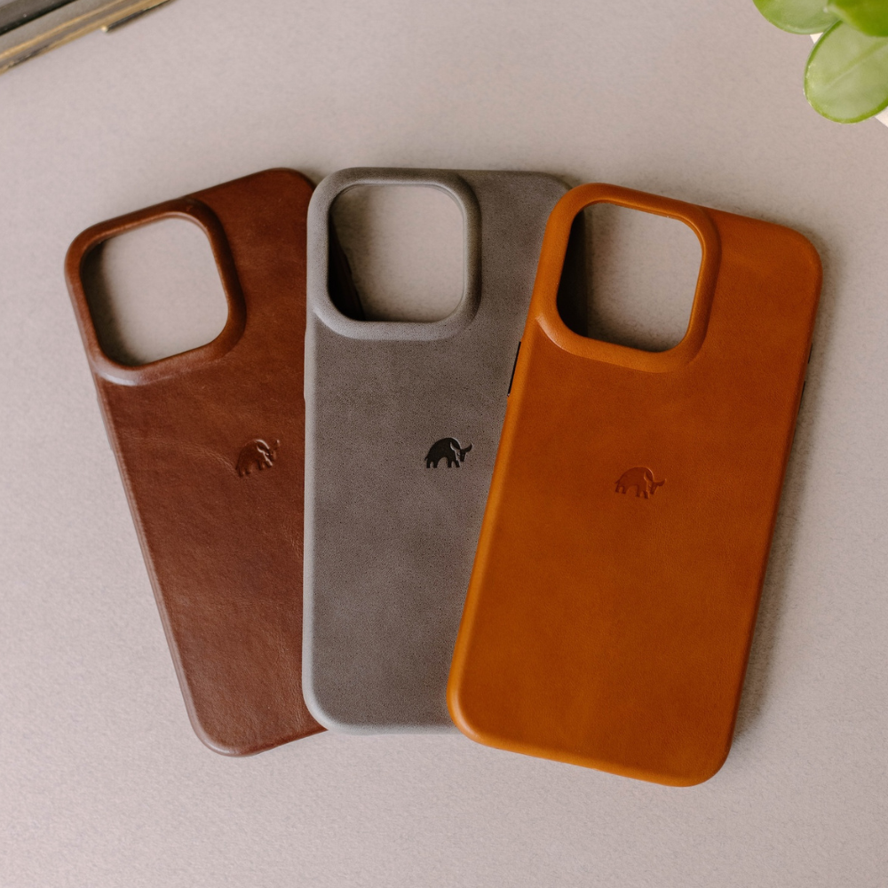 Three leather smartphone cases (brown, gray, tan) with small embossed elephant logo, arranged overlapping on a light surface.