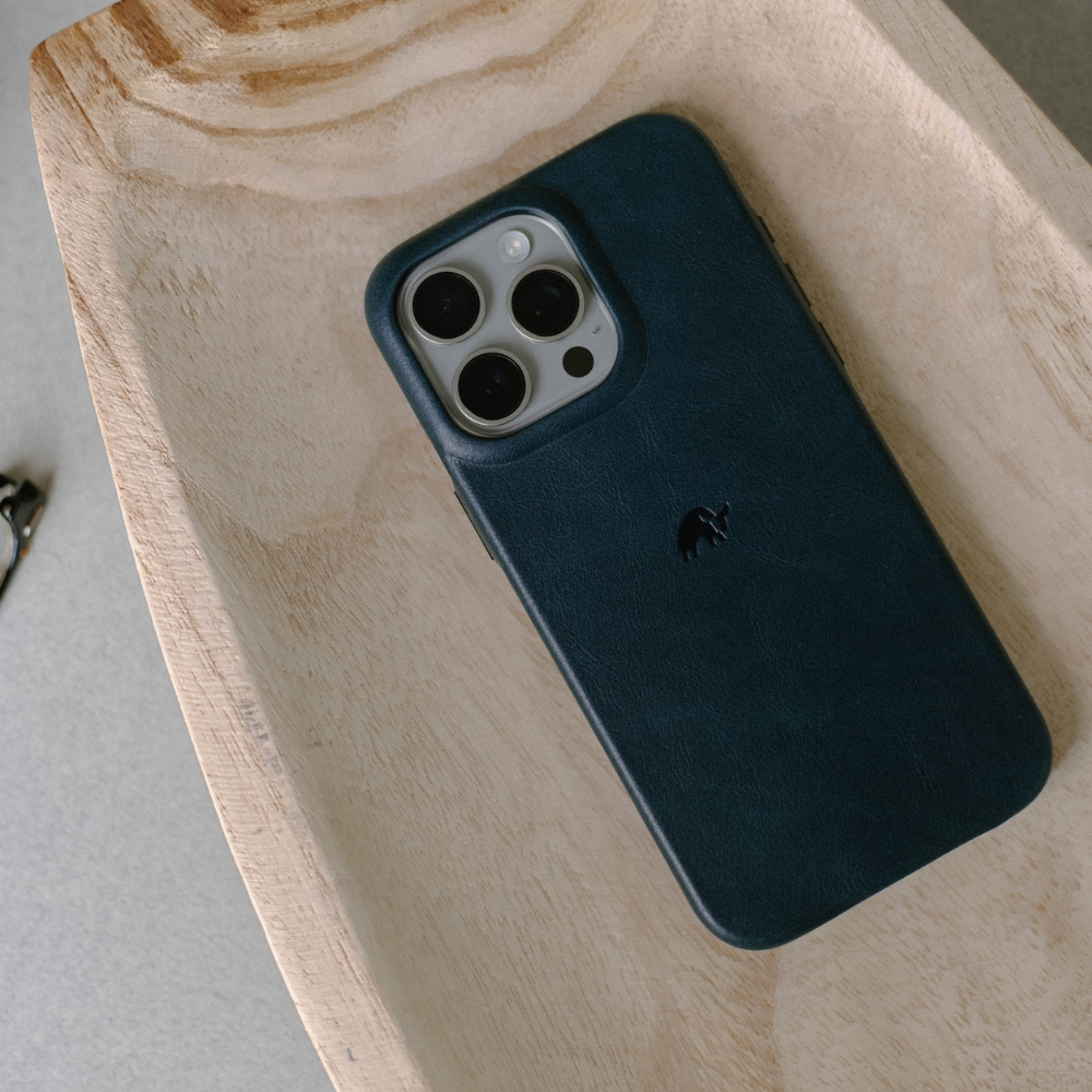 Dark leather-covered smartphone with triple camera module resting in a light wooden tray.