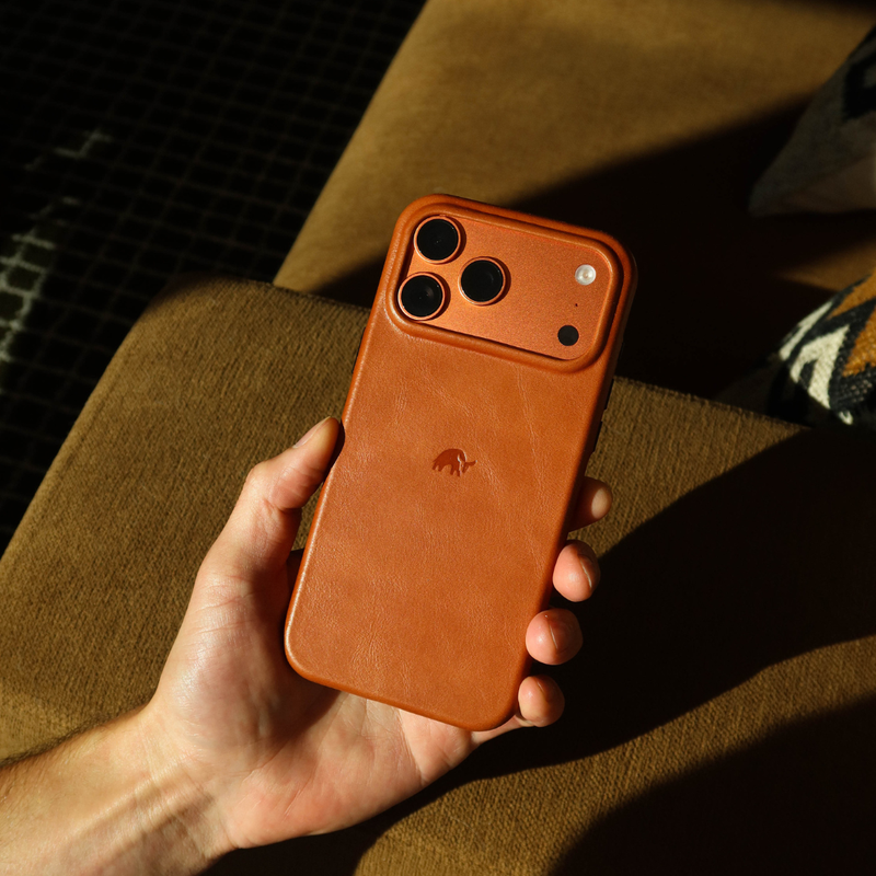 Hand holding back view of Plateau case in sienna leather showing raised camera plateau and embossed logo on brown fabric